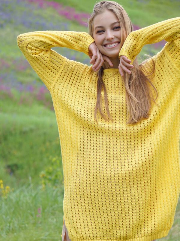 A beautiful yellow lace tunic dress with a loose fit and long sleeves, perfect for summer days. The dress features intricate lace detailing on the sleeves and hemline, adding a touch of elegance to the casual style. The model is standing in field, surrounded by greenery and flowers, showcasing the dress in a natural setting.